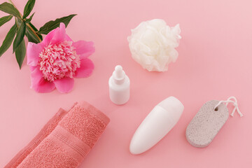 Towel with body care products and a peony flower on the pink background.