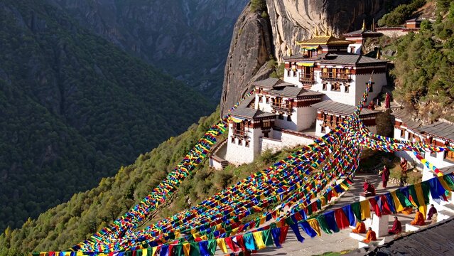 Colorful prayer flags decorating the hillside of taktsang monastery in paro valley, bhutan, as monks gather in celebration, highlight the vibrant spirituality against the himalayan backdrop