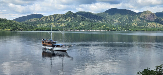Phinisi boat sailing in the Flores sea of the Komodo national park with mountain island background.