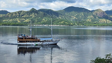 Phinisi boat sailing in the Flores sea of the Komodo national park with mountain island background.