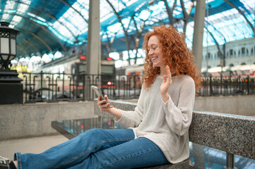 Happy tourist woman video calling with smartphone at train station