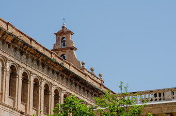 Elegant architectural detail of an old European church with a classic bell tower, surrounded by clear blue sky and green tree branches, perfect for travel and history themes.