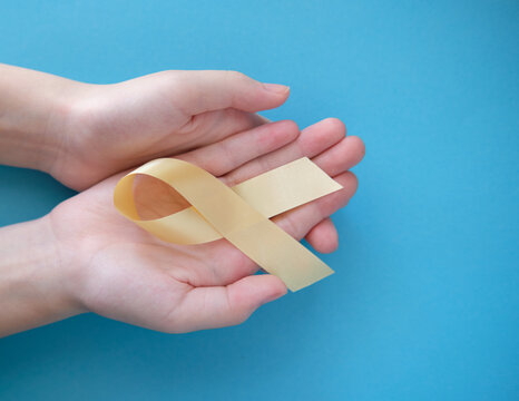 Gold symbolic ribbon - the problem of childhood cancer. Two crossed hands on a blue background