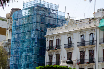 Architectural scene of an ornate historic building under renovation, covered with scaffolding and mesh in a European city. Urban restoration, construction site.