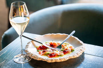 An elegant plate of salmon salad garnished with fresh herbs, served alongside a glass of sparkling white wine, set on a beautiful table.
