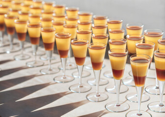 Layered yellow red fruit cocktails in wine glasses. Organized preparation for big happy hour party in buffet for big company. Long evening shadows