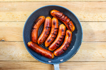 grilled sausages in a frying pan, on a wooden table