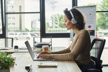 Focused professional working at a modern office desk with headphones and laptop during the day