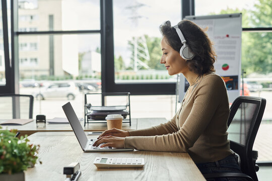 Focused professional working at a modern office desk with headphones and laptop during the day