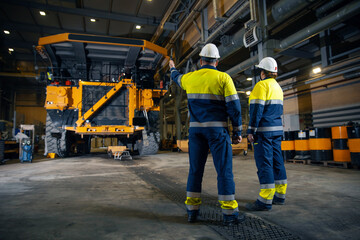 Two engineers control repair of dump car in garage of factory. Industry big yellow mining truck...