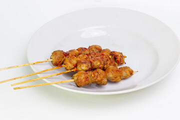 A plate of meat skewers with a white background. The skewers are arranged in a neat row and appear to be seasoned with chili