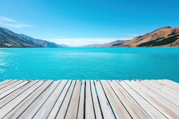 A wooden dock overlooks a calm turquoise lake surrounded by distant mountains under a clear blue sky.