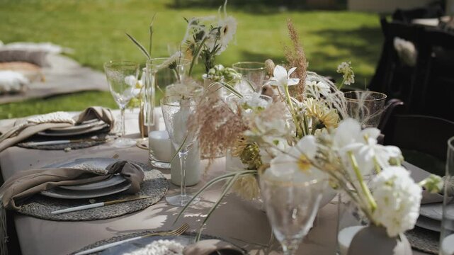 Outdoor wedding decor. Elegantly decorated outdoor dining table decorated with beautiful floral decor. Glasses, plates, cutlery, napkins. Celebration dinner or party.