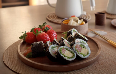 Fresh sushi rolls with strawberries and pickled vegetables served on a wooden plate in a cozy dining setting
