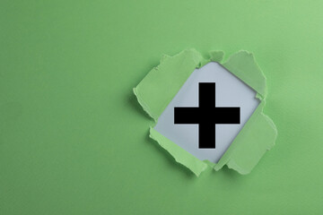 Black plus sign symbol revealed through torn green paper concept for positive symbol, creative...