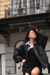 Obraz premium Stylish Asian woman posing on city streets in fashionable outfit. Confident urban look, modern lifestyle, street fashion and beauty concept, diversity and individuality.