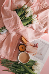 Cup of coffee, burning candle, and fashion magazine on bed with pink denim jacket and white tulips...