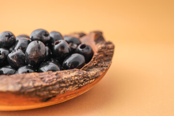 Rustic wooden bowl filled with shiny black olives on warm brown background. Organic healthy snack in natural serving dish. Minimalist food presentation with earthy tones