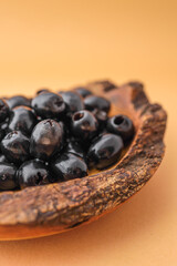 Rustic wooden bowl filled with shiny black olives on warm brown background. Organic healthy snack in natural serving dish. Minimalist food presentation with earthy tones