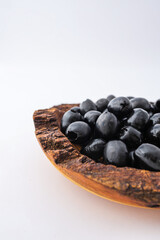 Rustic wooden bowl filled with glossy black olives placed on a clean white background. Minimalist food concept with natural textures and healthy organic snack