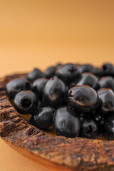 Rustic wooden bowl filled with shiny black olives on warm brown background. Organic healthy snack in natural serving dish. Minimalist food presentation with earthy tones