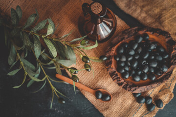 Top view of rustic composition with black olives in a wooden bowl, a wooden spoon, a glass bottle...