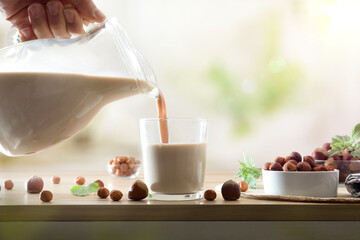 Filling glass with hazelnut drink on wooden kitchen bench