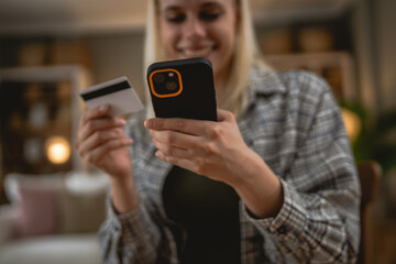 Young woman using smart phone shopping online holding credit card home