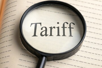 Tariffs and diplomacy shape trade agreements concept. Magnifying glass focusing on the word "Tariff" in a lined notebook.