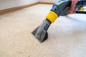 Carpet cleaning with vacuum extractor held by adult male hand