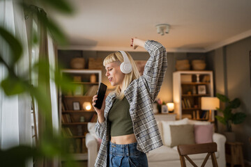 Young woman with headphones listen music and sign on mobile phone happy