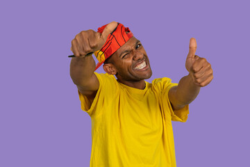 Enthusiastic man showing thumbs up and pointing finger gun gesture on purple background