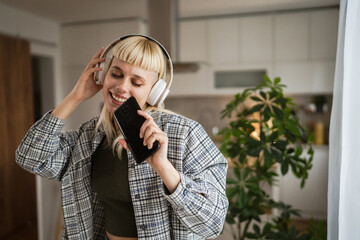 Young woman with headphones listen music and sign on mobile phone happy