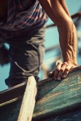A close-up image of a man's hand on weathered wooden surface, working on construction.