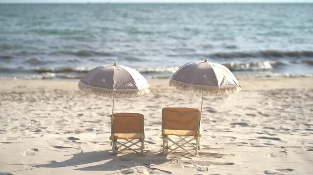 Beach Chairs Under a Parasol two matching beach chairs,children's size.A fringed parasol is set up above them, providing shade.The chairs face the calm ocean under a blue sky with some clouds.