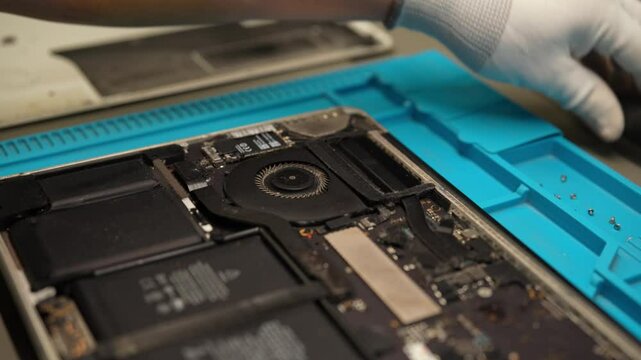 Skilled technician repairing laptop motherboard, disassembling electronic components with screwdriver in professional workshop, close-up. Concept of computer hardware, repairing, upgrade, technology.