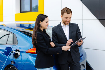 Smiling woman standing at the car and pointing at car seller tablet. She is picked right car for...