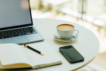 A clean white desk holds a cup of coffee, an open notebook, and a sleek minimalist laptop—ready for a calm and focused workspace.