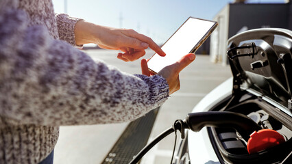 Close-up of woman's hand using smartphone app to charge electric car at ev station - smart green technology, eco-friendly transport and digital convenience concept.