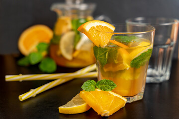 Orange lemonade in a transparent glass with straws and orange slices in front on a blurred dark...