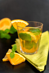 Glass of mint orange lemonade on napkin with orange slices in front on blurred dark background....