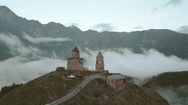 Stepantsminda, Georgia - 8th september, 2024: aerial rising view Stepantsminda, Gergeti, Georgia. Famous Gergeti Trinity Tsminda Sameba Church with autumn misty mountains landscape. Suv Near Church