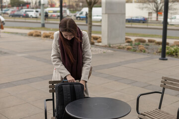 Obraz premium A woman is standing next to a table that has a backpack placed on it, observing her surroundings thoughtfully as she waits patiently