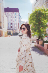 A business lady walks in the background of the city lit by the summer sun.