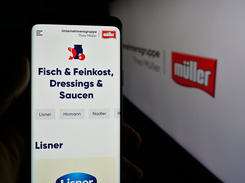Stuttgart, Germany - 04-24-2025: Person holding cellphone with web page of dairy company Unternehmensgruppe Theo M&uuml;ller on screen in front of logo. Focus on center of phone display.