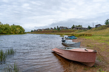 Boats on the river bank against the backdrop of log houses and an old wooden church.