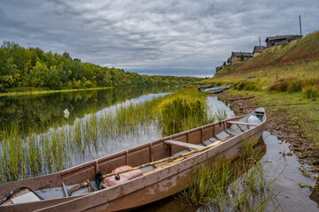 Boats on the river bank against the backdrop of log houses and an old wooden church.