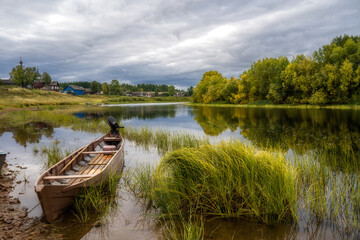 Boats on the river bank against the backdrop of log houses and an old wooden church.