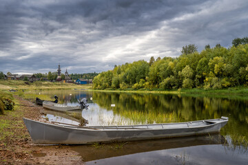 Boats on the river bank against the backdrop of log houses and an old wooden church.