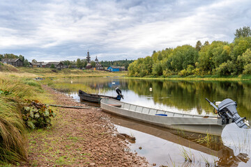 Boats on the river bank against the backdrop of log houses and an old wooden church.